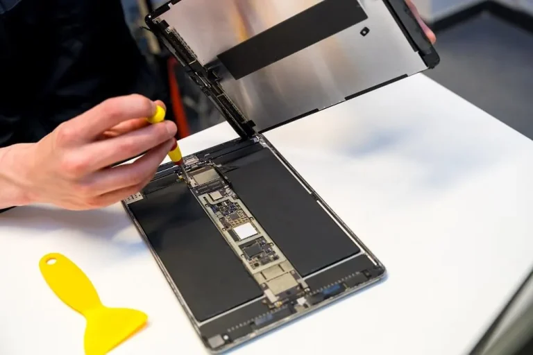 Technician repairing a tablet on a clean white workbench using precision tools