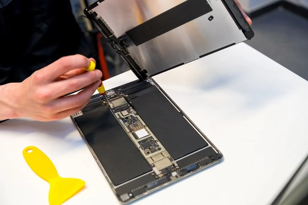 Technician repairing a tablet on a clean white workbench using precision tools