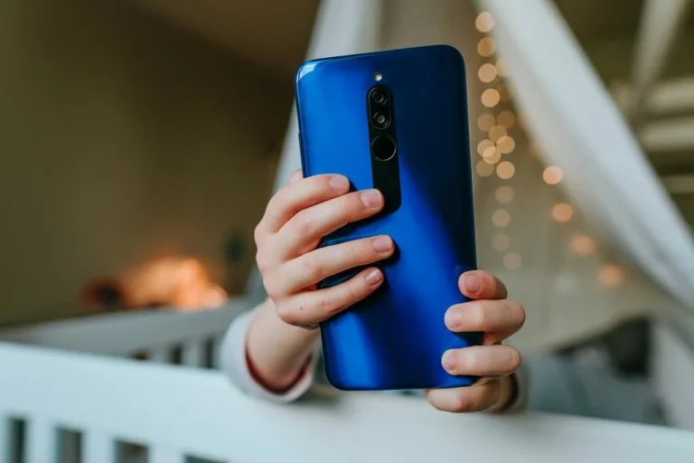 Child holding a Xiaomi phone while sitting safely in a crib at home, exploring a mobile device